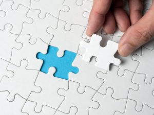 Hand completing the last piece of puzzle on blue background